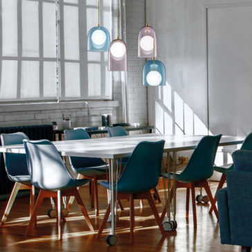 Contemporary Long Glass Dome Pendant Light A contemporary dining area with a long white table surrounded by teal chairs. Above the table, four Contemporary Long Glass Dome Pendant Lights with colorful shades hover gracefully from the ceiling. The room features expansive windows with shades, white brick walls, and wooden floors.