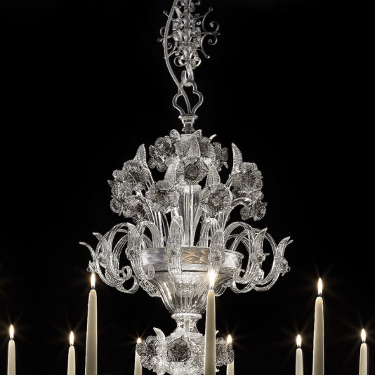 Ornate Floral Glass Chandelier With Candle Details The Ornate Floral Glass Chandelier With Candle Details, featuring intricate floral designs, shines brilliantly against a dark backdrop. Several lit candles arranged around it cast a warm, inviting glow.