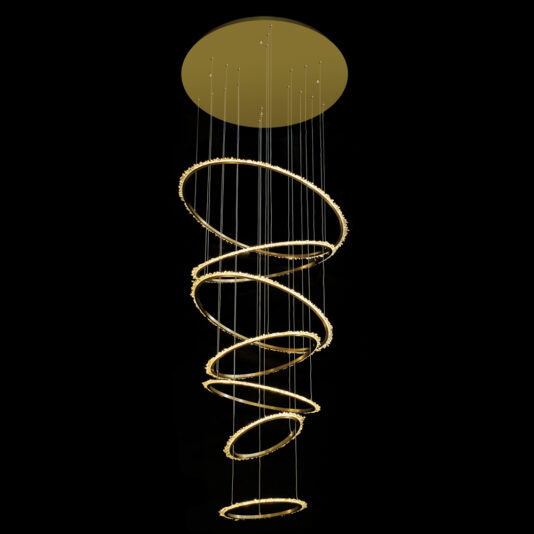 The Quartz Halo 7 Ring Gold Chandelier showcases a contemporary spiral design with golden rings of different sizes aligned horizontally. These rings, which are suspended by thin wires from a circular ceiling mount, emit a soft and warm light that lends an elegant and modern touch against dark backgrounds.