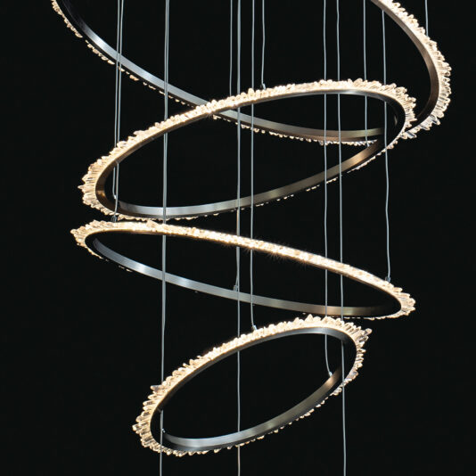 Quartz Crystal 7 Ring Nickel Chandelier The Quartz Crystal 7 Ring Nickel Chandelier is an artistic lighting fixture featuring multiple circular, metal rings suspended in a spiral arrangement. Adorned with small, glowing lights along its edge, it creates a cascading effect against a dark background.