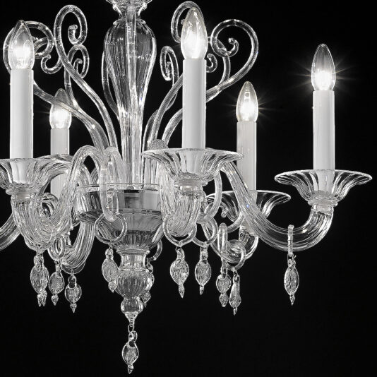 Small Traditional Clear Glass Chandelier A close-up view of the Small Traditional Clear Glass Chandelier shows multiple candle-like light bulbs. This clear glass chandelier features intricate glasswork with elegantly curving arms and shimmering hanging crystal ornaments, all set against a dark background.