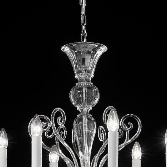 Small Traditional Clear Glass Chandelier A close-up of the Small Traditional Clear Glass Chandelier featuring a polished silver finish, intricate design elements, six candle-like lights, and an elegant central stem. The lights are turned on, emitting a soft, warm glow.