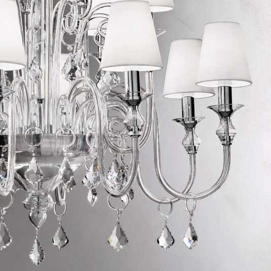 Traditional Chandelier With Crystal Drops A close-up view of the Traditional Chandelier With Crystal Drops reveals multiple silver arms, each adorned with sleek white lampshades. Numerous clear crystal pendants dangle elegantly from the fixture, reflecting light and adding a touch of sophistication to the design.