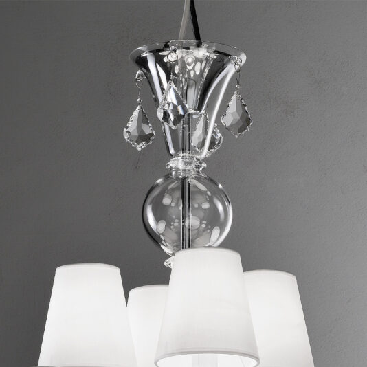 Traditional Chandelier With Crystal Drops Close-up of the Traditional Chandelier With Crystal Drops, showcasing its silver metallic design. The elegant fixture features hanging crystal ornaments and white fabric lampshades on its multiple light fixtures, all set against a plain, light gray wall.