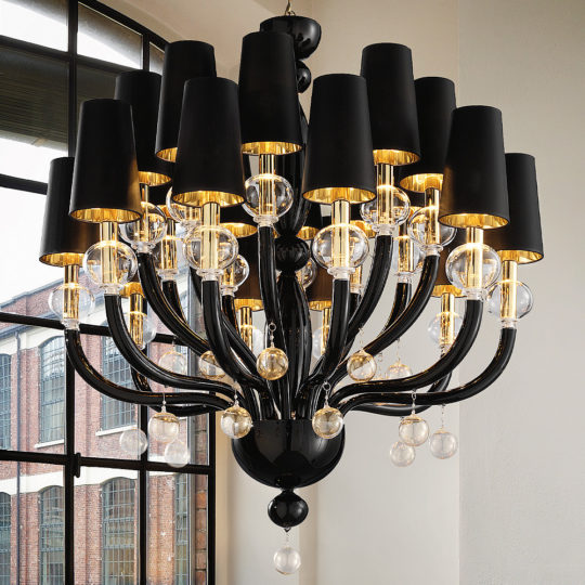 The Traditional Glass Orb Detail Chandelier with a Black Frame, adorned with elegant glass orbs and gold accents, is suspended in a stylish industrial space featuring a large, multi-paned window. This lighting fixture seamlessly combines modern and classic design elements.
