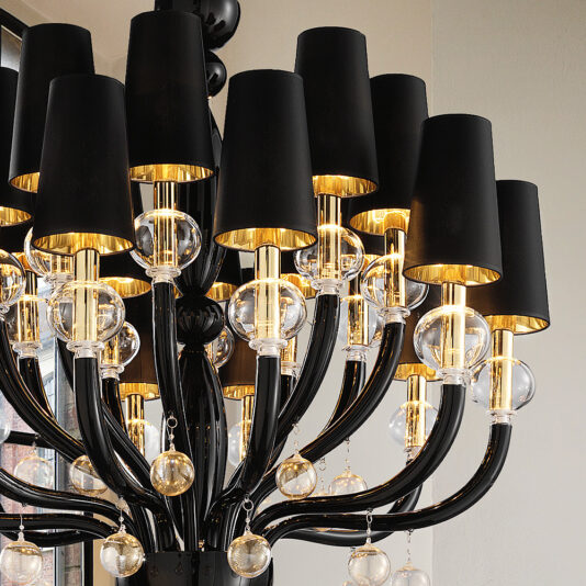 The Traditional Glass Orb Detail Chandelier With Black Frame, featuring multiple black-shaded lamps and clear glass orb accents, is elegantly suspended from the ceiling. The warm glowing lights illuminate the space with a sophisticated and contemporary design that complements both traditional and modern aesthetics.