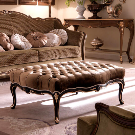 A luxurious living room featuring the Venetian Style Button Upholstered Coffee Table, characterized by its elegant button upholstery and intricately carved wooden legs. The room is completed with a plush, patterned sofa adorned with assorted throw pillows, a wooden console table, decorative vases, and a warmly lit ambiance.