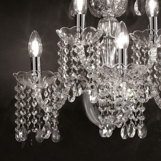 Classic Glass Wall Light With Crystal Drops A close-up of the Classic Glass Wall Light With Crystal Drops, showcasing lit bulbs with clear, ornate glass holders. The fixture is adorned with numerous strands of hanging crystals, reflecting and refracting the light to create a sparkling effect against a dark background.