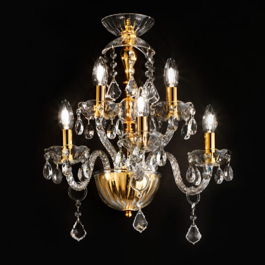 A luxurious, classic gold and crystal chandelier with intricate designs and multiple arms, each holding a lit candle-like light bulb. The chandelier features hanging crystal ornaments, adding an elegant and opulent touch against a dark background, reminiscent of the Classic Gold 5 Arm Wall Light With Crystal Drops.