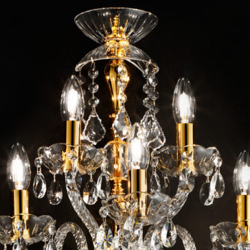 The Classic Gold 5 Arm Wall Light With Crystal Drops exudes a luxurious and timeless ambiance against a dark background, featuring several lit candle-shaped bulbs with a golden frame and crystal accents, including elegantly hanging teardrop-shaped crystals.