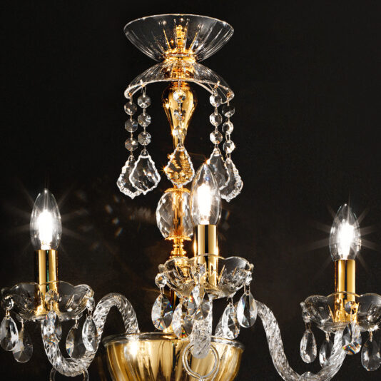 Classic Gold Wall Light With Crystal Drops A close-up image of an ornate chandelier featuring three lit bulbs. The chandelier, similar to the Classic Gold Wall Light With Crystal Drops, showcases gold and crystal elements with hanging crystal ornaments reflecting the light, creating a dazzling effect against a dark background.