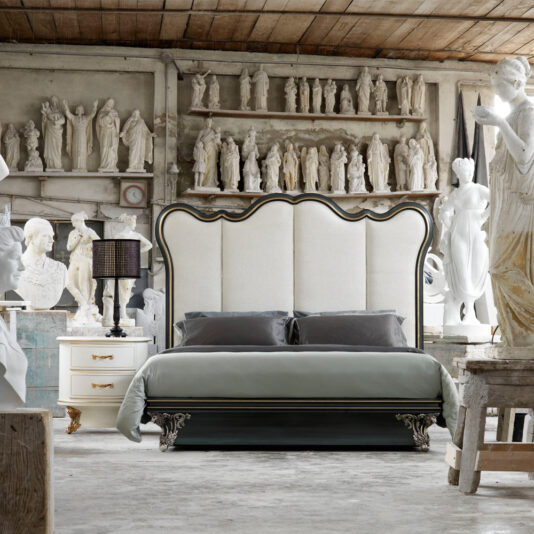 Classic Venetian Style Bed With Tall Headboard A bedroom featuring the Classic Venetian Style Bed With Tall Headboard, adorned with tall upholstered panels and intricate artistic carvings. Classical statues and busts surround the bed, accompanied by an ornate nightstand holding a lamp. The room exudes an artistic studio atmosphere, perfectly blending modern and classical elements.