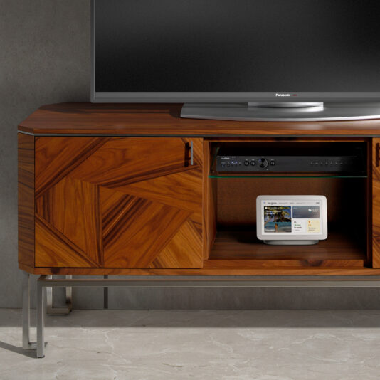 The Elegant Contemporary Veneer TV Unit features a sleek, modern design with cabinet doors adorned in a geometric pattern. Constructed from wood veneer and supported by sturdy metal legs, this unit serves as the perfect stand for your flat-screen TV while accommodating an electronic device with a display screen on one of its shelves. The setup is complemented by a minimalist gray wall background.