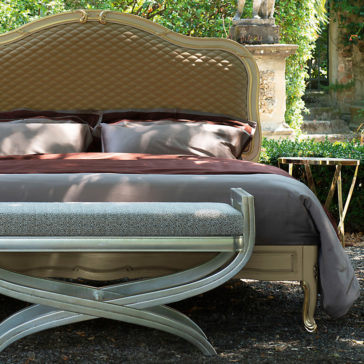 Elegant Ornate Classic Style Bed The Elegant Ornate Classic Style Bed, featuring a quilted headboard, is beautifully adorned with gray and brown bedding and pillows, situated outdoors in a lush garden. In front of the bed stands a bench with a patterned cushion and a metallic frame. The scene radiates elegance and tranquility.