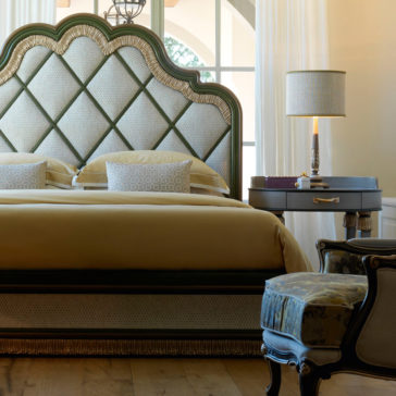 Elegant bedroom featuring the Exclusive Bed With Tassel Design Detail, complete with a large, tufted headboard adorned with green trim and fringe. The bed is neatly made with beige bedding and accented by two small decorative pillows. Matching nightstands with lamps flank either side, and a patterned armchair adds a touch of style. Large windows with white curtains allow natural light to flood the room.