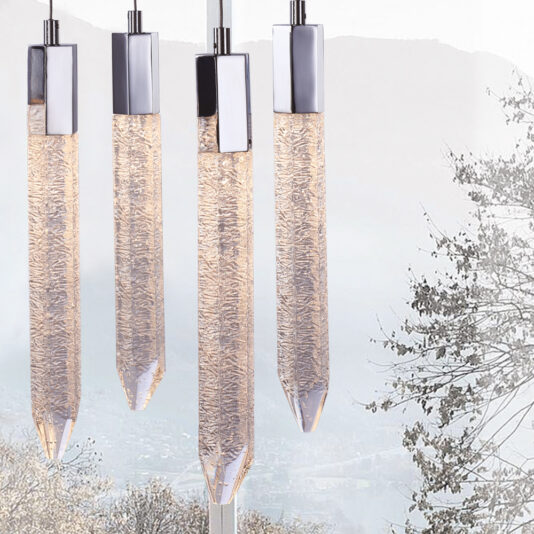 Exclusive Chrome Pendant Light Cluster Four modern pendant lights with elongated, textured glass shades and sleek chrome tops are artfully displayed against a softly blurred background of tree branches and a misty landscape. The Exclusive Chrome Pendant Light Cluster features uniformly aligned lights, exemplifying a minimalist and elegant design.