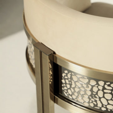 Exclusive Curved Bar Stool A close-up view of the Exclusive Curved Bar Stool, showcasing its beige seat and backrest. The metallic frame features an intricate, rock-like cutout pattern and boasts a modern, gold-colored finish.