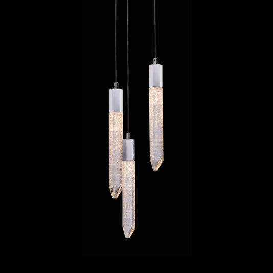 An Exclusive Triple Chrome Pendant Light, this modern fixture showcases three elongated, crystalline elements illuminated and suspended at varying lengths from sleek black cords against a dark background.