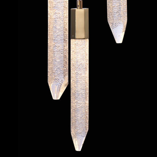 The Exclusive Triple Gold Pendant Light showcases three elongated, textured glass pieces that resemble icicles, suspended vertically against a black backdrop. Each piece tapers to a point at the bottom and is mounted on a metallic fixture at the top.