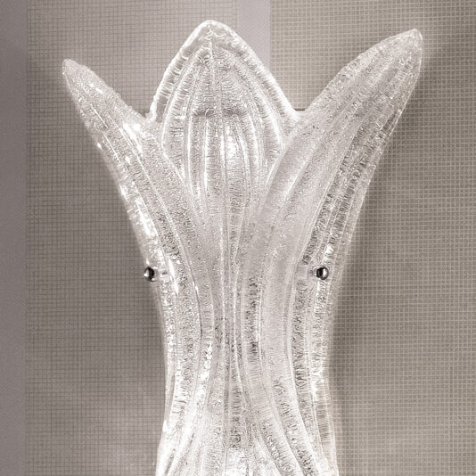 A close-up shot of the Glass Leaf Wall Light, showcasing its elaborate design with three curved, textured glass panels that converge at the top, resembling abstract flower petals or leaves. The background features a light gray textured wall.