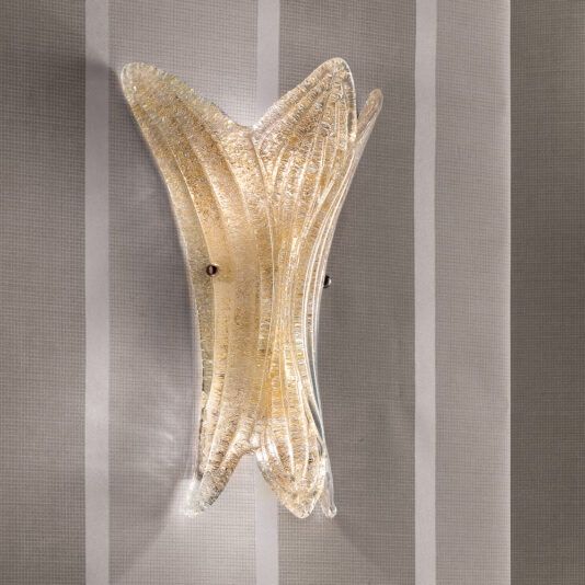 A Glass Leaf Wall Light featuring a curvy, translucent glass shape that emits a warm, golden glow is mounted on a wall with a subtle gray and white striped pattern, adding an elegant touch to the room with its modern design.