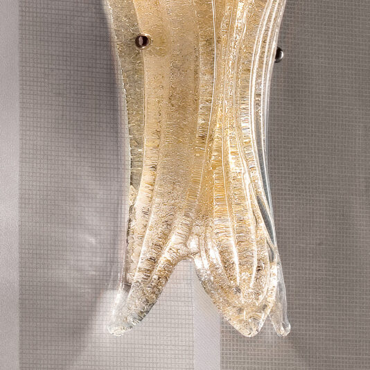 A close-up of the elegant Glass Leaf Wall Light, crafted from textured glass. The curved, flowing design of the glass resembles a stylized flower or leaf. The fixture emits a warm glow and is secured to a patterned wall with two metallic screws.