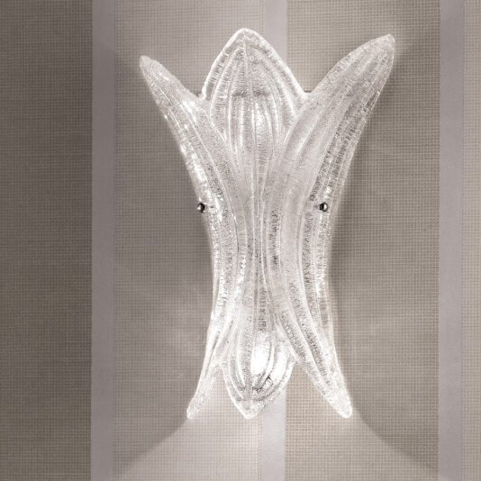 A contemporary Glass Leaf Wall Light is affixed to a patterned light gray wall. The sconce showcases an elegant, symmetrical design with curving, petal-like shapes that create a floral look. Soft light emanates from within, accentuating the textured surface.