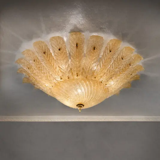 The Large Amber Glass Leaf Ceiling Light features a stunning design with fan-like segments radiating from a central fixture, creating intricate shadows that dance across the ceiling. Its elegant Art Deco motif emits a warm, ambient glow, and showcases an exquisite ceiling molding as well.