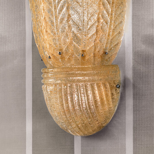 Large Amber Glass Leaf Wall Light A Large Amber Glass Leaf Wall Light with a textured design and ribbed, leaf-like details is mounted on a vertically striped wallpapered wall. The vintage wall sconce features subtle metallic screws that hold the intricate amber glass securely in place.