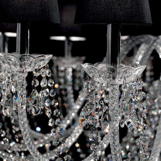 Large Crystal Chandelier With Shades Close-up of the Large Crystal Chandelier With Shades, showcasing its black lampshades. The chandelier boasts ornate glass arms and multiple hanging crystal prisms that reflect light, creating a sparkling effect. The dark backdrop emphasizes the chandelier's intricate details and brilliance.
