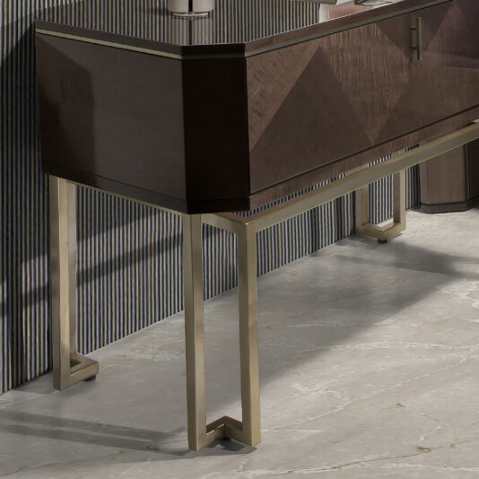 Large Dark Maple Bedside Table A modern console table with a dark wooden top featuring a sleek, geometric design and metallic legs with a reflective finish. Positioned against a striped wall and resting on a polished tile floor, this piece adds the same contemporary feel as the Large Dark Maple Bedside Table.