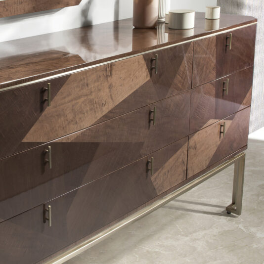 A sleek, modern Large Dark Maple Double Dresser with a glossy finish and geometric pattern is displayed against a neutral-toned wall. It features nine drawers, each adorned with small metallic handles. Minimalistic vases and cups adorn the top of the dresser, complementing the room's decor.