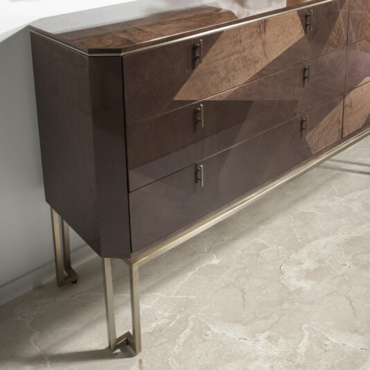 A modern wooden sideboard with a geometric design, featuring a pattern of angular light and dark wood accents reminiscent of the Large Dark Maple Double Dresser. The piece has gold-colored metal legs and handles and is set against a light-textured floor and a white wall.