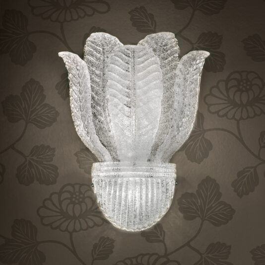 The Large Glass Leaf Wall Light features a frosted glass design that resembles a flower with petals. Mounted on an ornate dark wallpaper background adorned with floral patterns, the illuminated fixture highlights its intricate textures and details beautifully.