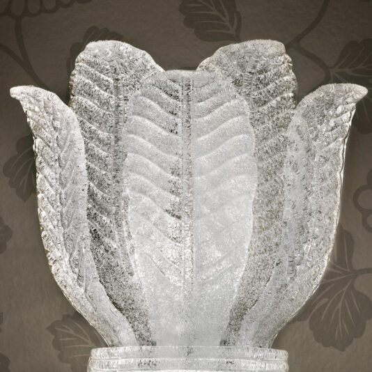 Large Glass Leaf Wall Light A detailed close-up capture of the Large Glass Leaf Wall Light, sculpted to mimic the natural elegance of plant leaves. The piece showcases a textured, frosted finish, set against a backdrop featuring a subtle dark floral pattern.