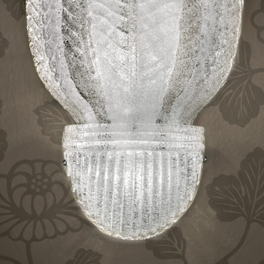 Large Glass Leaf Wall Light A textured Large Glass Leaf Wall Light with an etched leaf pattern is illuminated. The wall behind it is adorned with elegant brown floral wallpaper, adding a sophisticated touch to the image. Together, the light fixture and wallpaper create a warm and inviting ambiance.