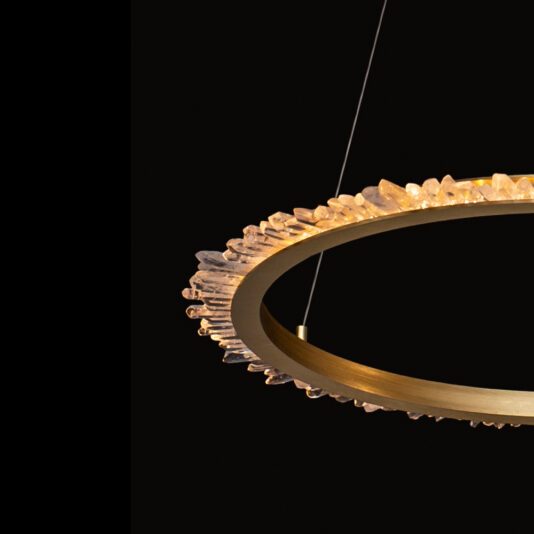 Large Quartz Crystal Gold Round Chandelier The Large Quartz Crystal Gold Round Chandelier features a gold-toned frame adorned with quartz crystal-like protrusions, suspended from a thin wire, set against a black background. The crystals encircle the light source, giving it a luxurious and elegant appearance.
