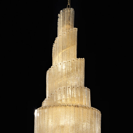 Large Tiered Amber Glass Chandelier The Large Tiered Amber Glass Chandelier, featuring multiple spiraling tiers, shines brilliantly against a black background. The glass tubes radiate a golden glow, creating a luxurious and elegant ambiance.