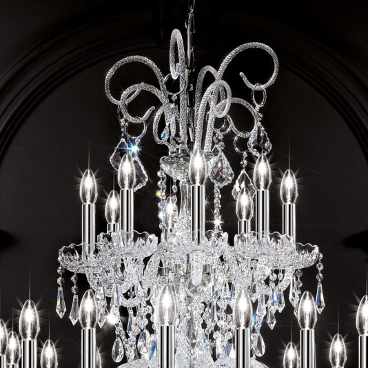 Large Two Tier Blown Glass Chandelier With Crystals The Large Two Tier Blown Glass Chandelier With Crystals, featuring multiple candle-shaped bulbs and intricate decorations including crystals, pendants, and swirls, is illuminated and sparkling against a dark background.