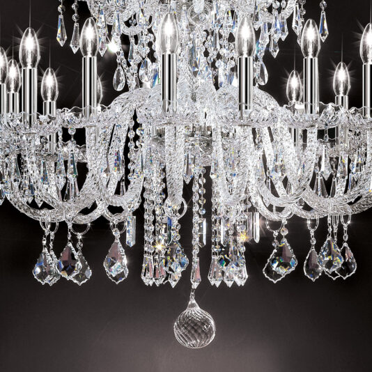 Large Two Tier Blown Glass Chandelier With Crystals A detailed close-up of the Large Two Tier Blown Glass Chandelier With Crystals showcases its elegance and size, featuring numerous candle-like bulbs, intricate glass arms, and dangling prism ornaments that catch and reflect light beautifully against a dark background.