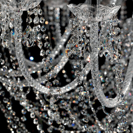 Close-up of the Large Two Tier Crystal Chandelier With Shades showcasing its intricate details. The chandelier features ornate crystal chains and dangling teardrop-shaped crystals that reflect light, creating a sparkling effect. Set against a dark background, the brilliance of the crystals is beautifully highlighted.