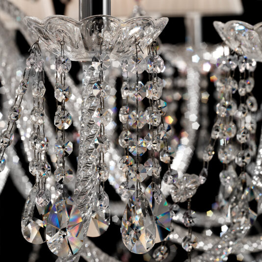 Close-up of the Large Two Tier Crystal Chandelier With Shades, highlighting its intricate detailing. The image features crystal beads, cut glass droplets, and faceted prisms, capturing light reflections and creating a sparkling effect. The background shows additional chandelier elements out of focus.
