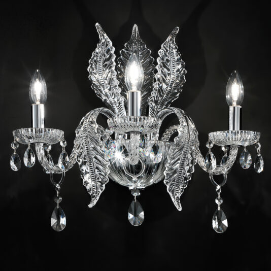 The Luxury Acanthus Triple Glass Wall Light is a sophisticated, three-arm crystal wall sconce adorned with detailed glass leaves and hanging crystal pendants. Each arm supports a candle-style light bulb that emits a gentle glow, with the dark background accentuating the acanthus-inspired elegance and intricate design of this exquisite lighting piece.