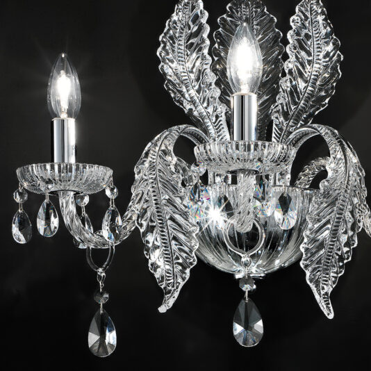 Luxury Acanthus Triple Glass Wall Light A close-up shot of an ornate crystal chandelier with two lit bulbs, reminiscent of the Luxury Acanthus Triple Glass Wall Light, features intricate leaf-shaped crystal designs and several hanging crystal ornaments, set against a dark background. The crystals reflect and refract the light beautifully.