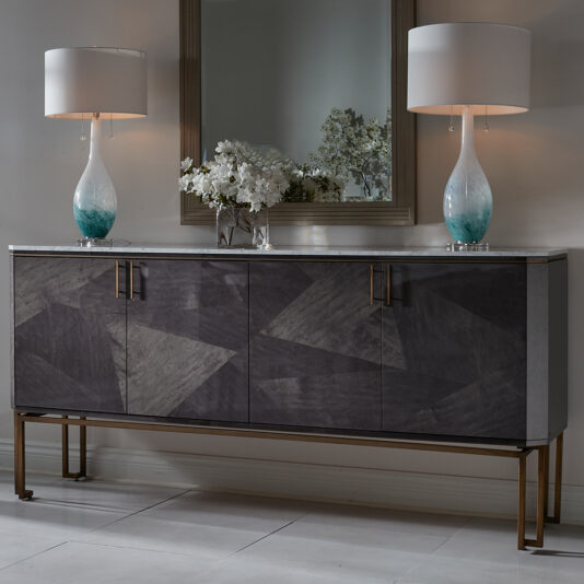 This sophisticated Luxury Marble Top Veneer Sideboard features a geometric patterned dark wood veneer and is adorned with two stylish blue and white gradient table lamps alongside a floral arrangement. A large mirror above it reflects the elegance, while the sideboard, with its sleek metal legs, rests on a polished white marble floor.