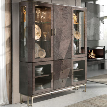 Luxury Brown Maple Veneer Display Cabinet A luxury brown maple veneer display cabinet with glass doors and a modern design stands tall in a contemporary living room. The top section showcases glassware and decorative items, while the bottom section holds dinner plates and bowls. The cabinet is elevated on sleek metallic legs.