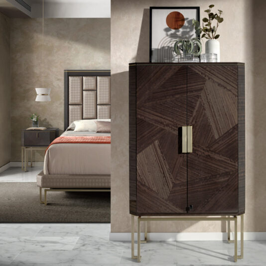 A modern bedroom showcases the Luxury Olive Veneer Jewellery Armoire, distinguished by its geometric patterns and metallic handles, elegantly topped with plants and framed art. The background reveals a bed dressed in earthy-colored linens and illuminated by a pendant light. The room is complete with a marble floor and neutral walls.