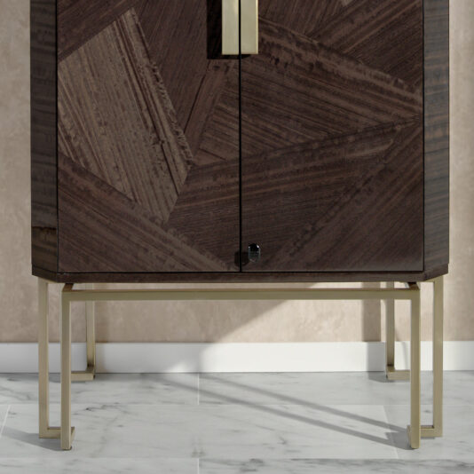 The Luxury Olive Veneer Jewellery Armoire is a modern wooden cabinet adorned with an intricate geometric design on its front and a sleek central handle. This exquisite piece stands on thin, gold-colored metal legs and is showcased against a beige textured wall, resting elegantly on a white marble floor.