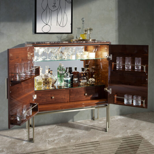 A modern, luxury Luxury Rosewood Veneer Drinks Cabinet featuring a marble countertop, neatly displaying an assortment of bottles both on top and within its compartments. The doors and shelves provide storage for glasses. The backdrop is adorned with a light grey wall highlighting a minimalist abstract portrait.