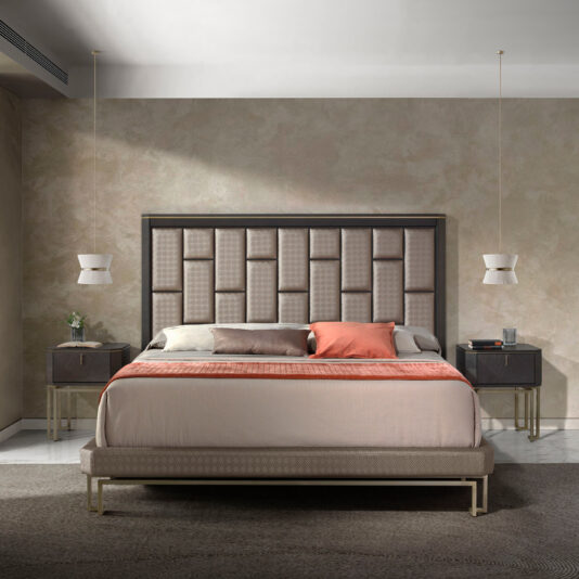 A modern bedroom showcases the Luxury Panel Upholstered Bed, which features a tall, square-patterned headboard. The bed is adorned with neutral and rust-orange linens and flanked by two dark wooden nightstands, each illuminated by hanging pendant lights above them. The textured walls are finished in neutral tones.
